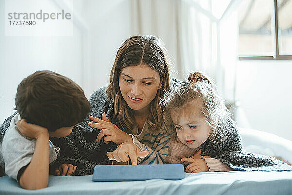 Junge Frau zeigt Kindern zu Hause im Bett einen Tablet-PC