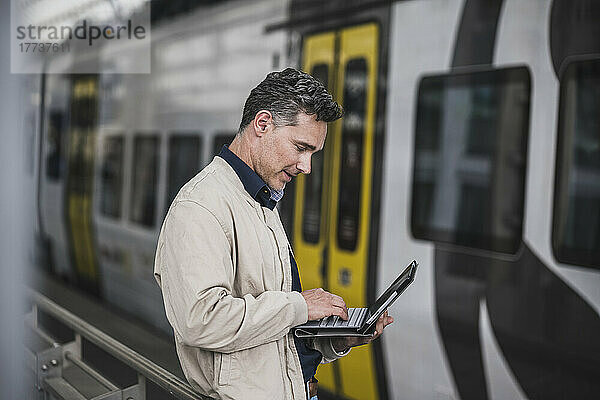 Reifer Geschäftsmann mit Tablet-PC vor dem Zug am Bahnhof