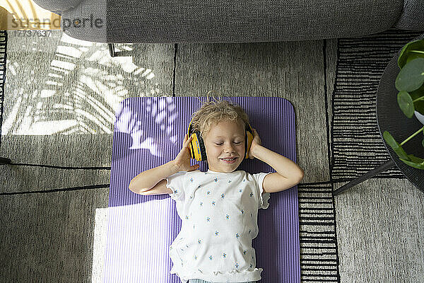 Girl listening music through headphones lying on exercise mat at home