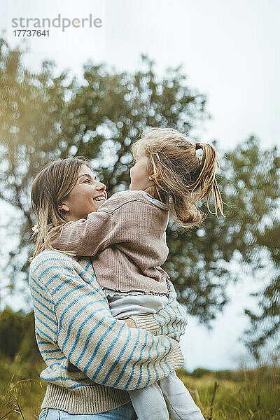 Lächelnde Mutter umarmt Tochter auf der Wiese