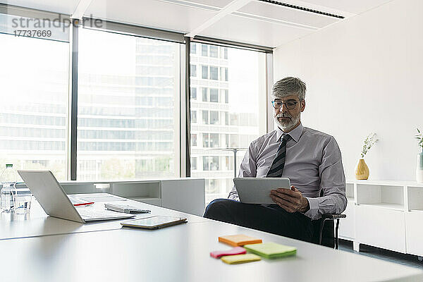 Geschäftsmann sitzt mit Tablet-PC auf Stuhl im Büro