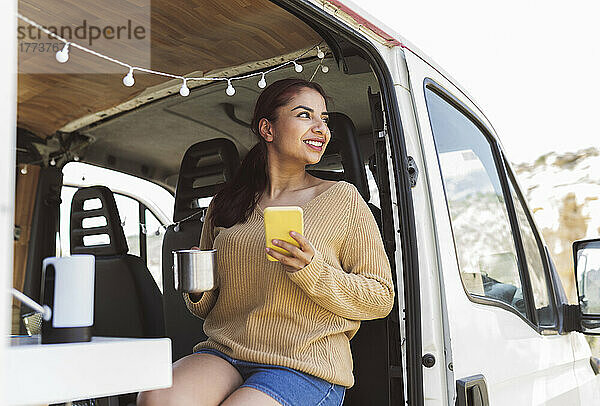 Lächelnde Frau mit Smartphone sitzt im Wohnmobil