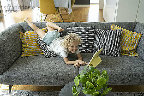 Mädchen mit Tablet-PC liegt zu Hause auf dem Sofa im Wohnzimmer