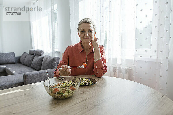 Frau isst Salat am Holztisch zu Hause