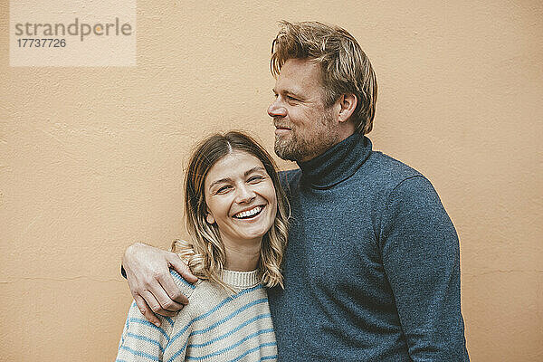 Lächelnder Mann umarmt Frau vor brauner Wand