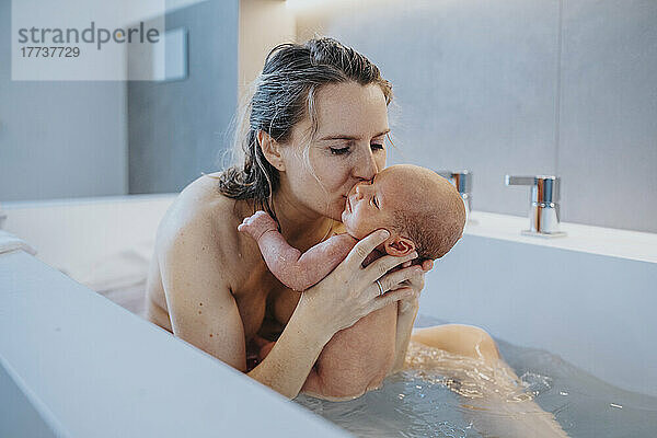 Woman kissing baby boy in bathtub at home