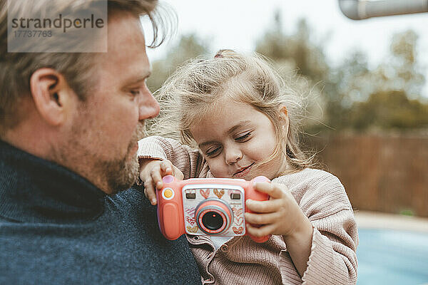 Father carrying daughter playing with toy camera