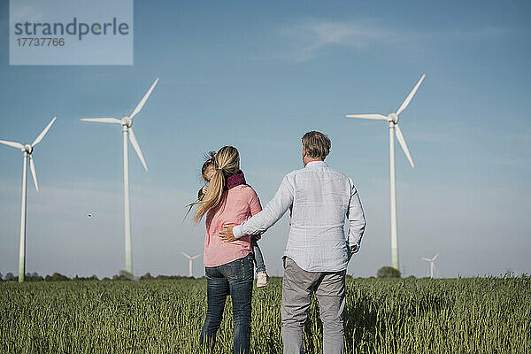 Frau mit Tochter steht an sonnigem Tag neben Mann im Windpark