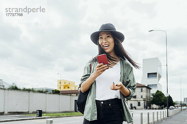 Happy woman wearing hat standing with mobile phone