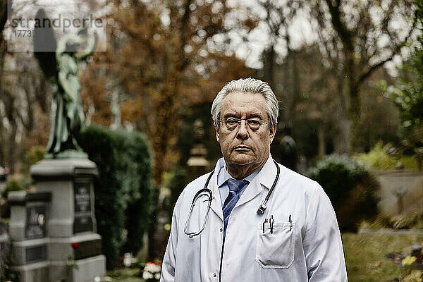 Leitender Arzt im Laborkittel steht auf dem Friedhof