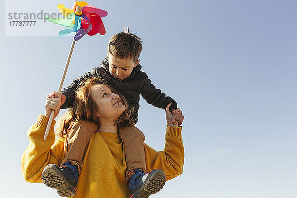 Glückliche Frau trägt Sohn auf Schultern vor blauem Himmel