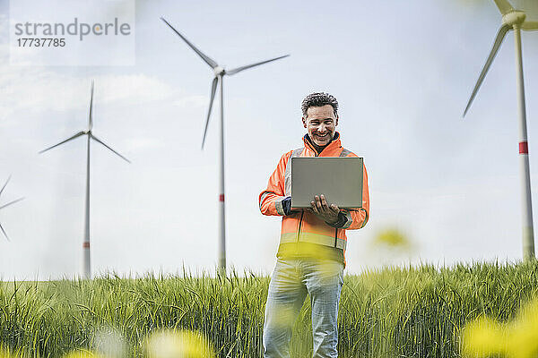 Glücklicher Ingenieur mit Laptop  der auf dem Feld steht