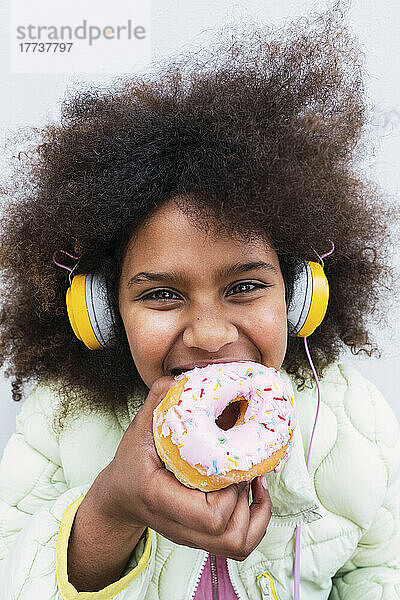 Afro-Mädchen mit Kopfhörern isst Donut