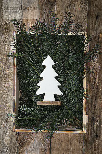 Wooden Christmas tree decoration lying in crate filled with conifer twigs