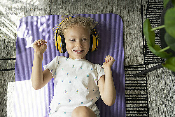 Smiling girl enjoying music through wireless headphones lying on exercise mat at home