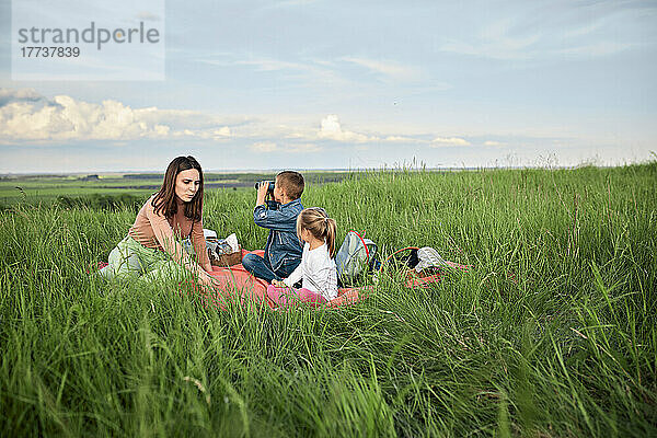 Mutter mit Kindern sitzt inmitten von Gras auf dem Feld