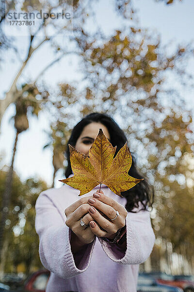 Junge Frau hält Herbstblatt im Park