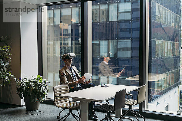 Geschäftsmann mit Virtual-Reality-Simulator sitzt auf einem Stuhl am Fenster im Büro