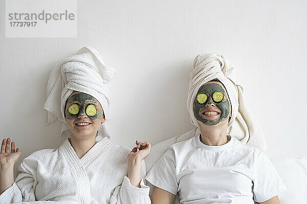 Happy young friends wearing facial masks relaxing at home