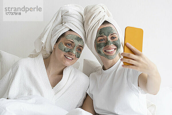 Fröhliche Freunde mit Gesichtsmasken machen Selfies per Smartphone