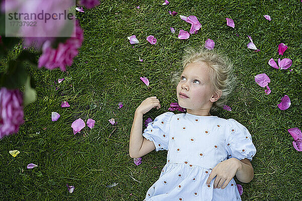Nachdenkliches süßes Mädchen liegt auf Gras im Rosengarten