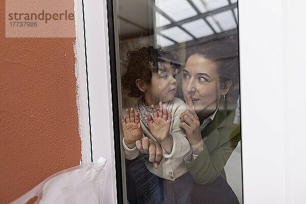 Mother and daughter looking through window