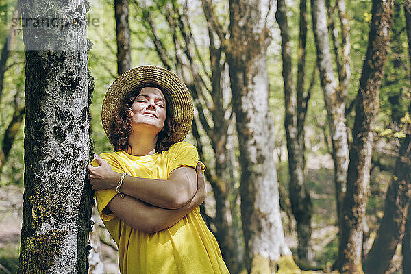 Frau mit Hut umarmt sich an einem sonnigen Tag am Baum