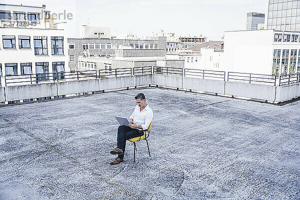 Geschäftsmann sitzt mit Laptop auf der Terrasse des Gebäudes