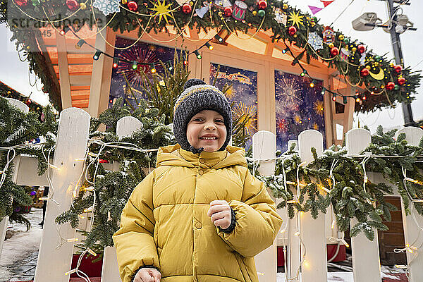Netter lächelnder Junge mit Strickmütze auf dem Weihnachtsmarkt