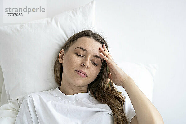 Tired woman with eyes closed lying on bed at home