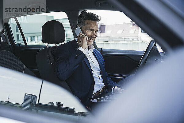 Glücklicher Geschäftsmann  der auf dem Fahrersitz im Auto sitzt und auf dem Smartphone spricht