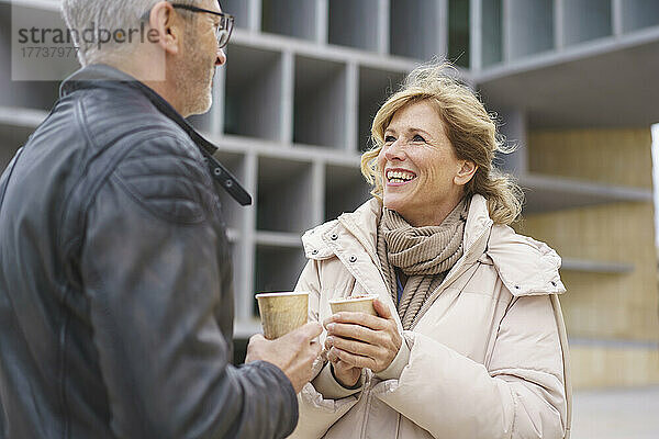 Glückliche Frau und Mann mit Einwegkaffeetasse stehen vor dem Gebäude