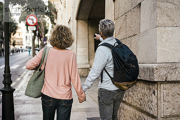 Älteres Paar hält sich an den Händen und geht im Urlaub auf dem Fußweg