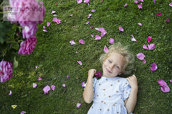 Smiling girl holding rose lying on grass at garden