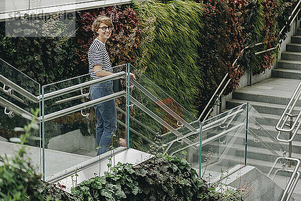 Lächelnde Frau steht am Glasgeländer auf der Treppe
