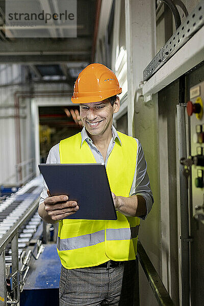 Lächelnder Arbeiter mit Schutzhelm und Tablet-PC im Lager