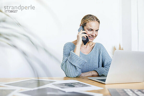 Lächelnde Geschäftsfrau  die zu Hause mit einem Laptop telefoniert und telefoniert
