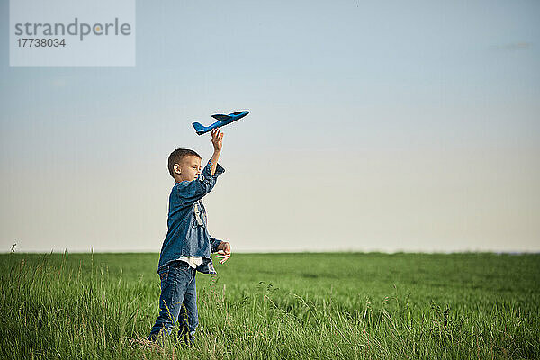 Junge wirft am Wochenende Flugzeugspielzeug in Feld