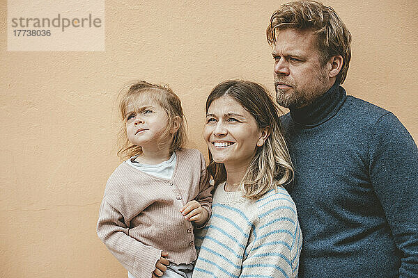 Lächelnde Mutter und Vater mit Tochter vor brauner Wand