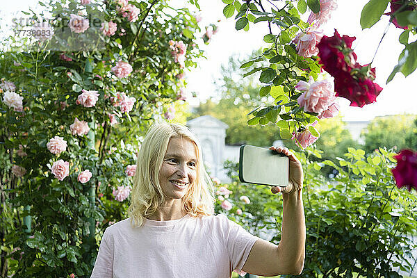 Lächelnde Frau macht Selfie per Smartphone im Rosengarten