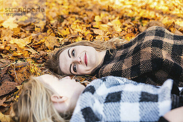Smiling woman looking at daughter lying on autumn leaves in park
