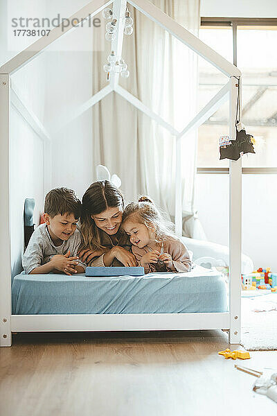Lächelnde junge Frau mit Kindern blickt auf den Tablet-PC  der im Bett liegt