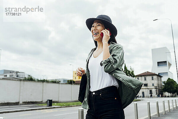 Fröhliche junge Frau mit Hut  die auf dem Smartphone spricht
