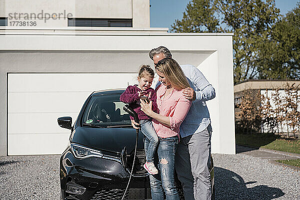 Frau zeigt Tochter  die an sonnigem Tag neben Mann steht  ihr Mobiltelefon