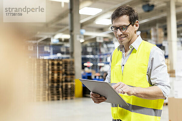 Lächelnder Arbeiter mit Brille und Tablet-PC im Lager