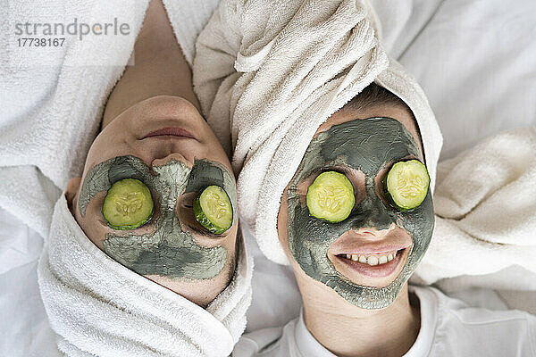 Happy friends wearing facial masks relaxing on bed at home