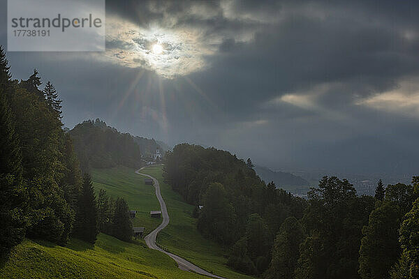 Deutschland  Bayern  Wamberg  Bewölkter Himmel über einer kleinen Straße  die zu einem abgelegenen Dorf im Wettersteingebirge führt