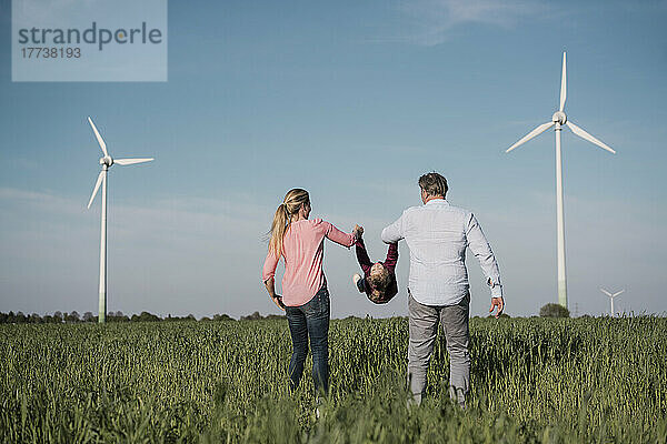 Verspielte Eltern schwingen ihr Mädchen an einem sonnigen Tag auf dem Feld