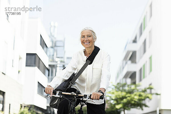 Fröhliche reife Geschäftsfrau pendelt mit dem Fahrrad