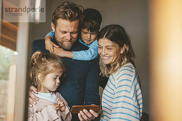 Glücklicher Mann teilt Smartphone mit Familie  gesehen durch das Fenster